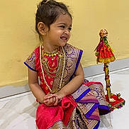 Meera joined the competition — help win amazing prizes! child, girl, traditional_clothing, sari, jewelry, smiling, sitting, floor, indoor, decorative_stick, cultural, portrait, young_child, happy, earrings, hair_tied, red_dress, gold_pattern, purple_border, marble_floor