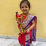Meera is registered to the contest to win money with this photo: child, girl, smiling, traditional_clothing, jewelry, barefoot, indoor, yellow_wall, tiled_floor, decorative_staff, happy, portrait, cultural, festive, colorful, standing, person, hair, accessories, celebration