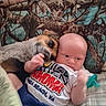 baby, dog, blanket, camo_pattern, bed, pacifier, infant, pet, snuggling, comfort, cute, animal, child, laying_down, clothing, indoor, friendship, affection, portrait, relaxation