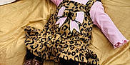 Sophia is registered to the contest to win money with this photo: baby, child, infant, bedspread, leopard_print, dress, pink_shirt, black_headband, boots, black_leggings, smile, happy, lying_down, indoors, cute, fashion, accessory, toddler, person, portrait