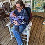 Sophia is registered to the contest to win money with this photo: woman, baby, child, rocking_chair, porch, wooden_floor, cushion, glasses, sneakers, purple_clothing, headband, sleeping, holding, wicker_chair, earrings, casual_wear, window, door, home_interior, outdoor