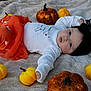 baby, infant, halloween, pumpkin, orange_clothing, white_clothing, black_headband, toy_spider, blanket, soft_texture, festive, autumn, cute, lying_down, decorations, holiday, child, small_pumpkins, sparkly_pumpkins, indoors