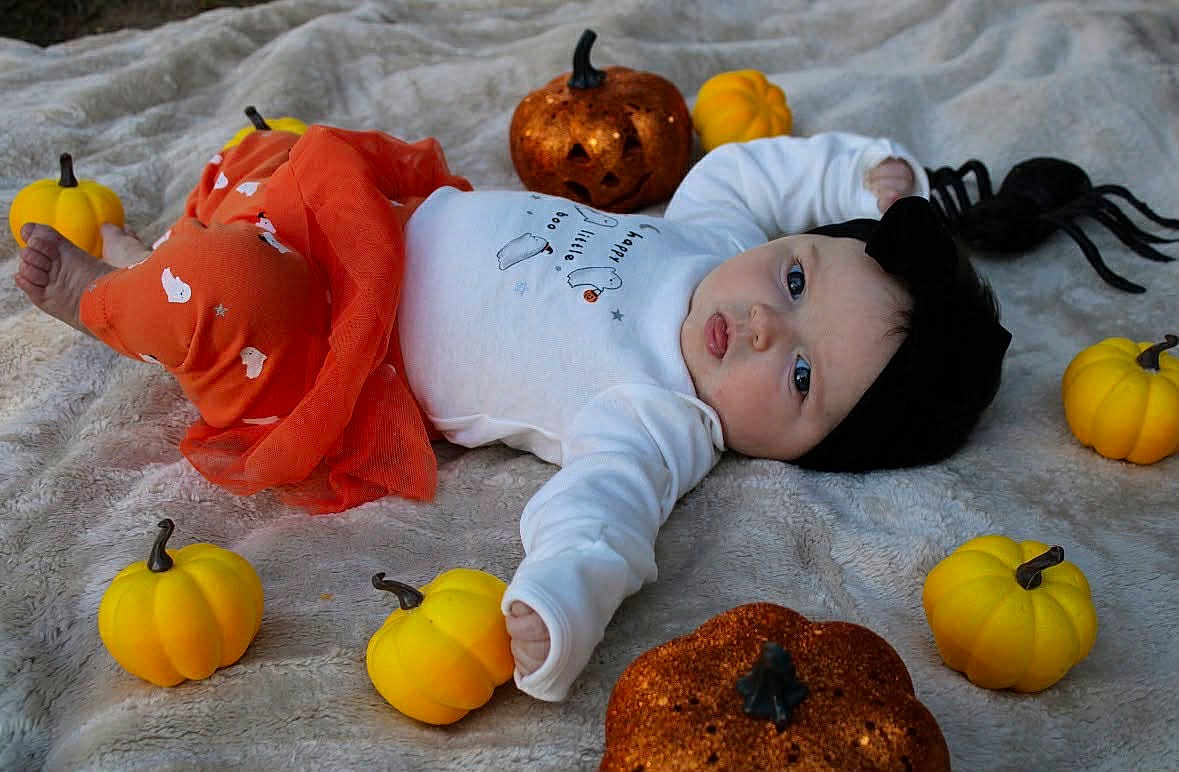Sophia joined the competition — help win amazing prizes! baby, infant, halloween, pumpkin, orange_clothing, white_clothing, black_headband, toy_spider, blanket, soft_texture, festive, autumn, cute, lying_down, decorations, holiday, child, small_pumpkins, sparkly_pumpkins, indoors