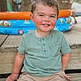 toddler, child, smiling, green_shirt, shorts, outdoor, wooden_steps, inflatable_pool, summer, happy, face, portrait, casual_clothing, blush, playful, daylight, skin, hair, person, sitting