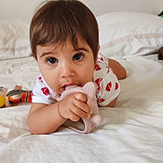 Yana participe au concours pour gagner de l'argent avec cette photo : baby, bed, casual_clothing, child, close_up, curious, face, hand, indoor, large_eyes, lying_down, person, pink_toy, plush_toy, short_hair, skin, soft_light, teething_toy, toddler, white_bed