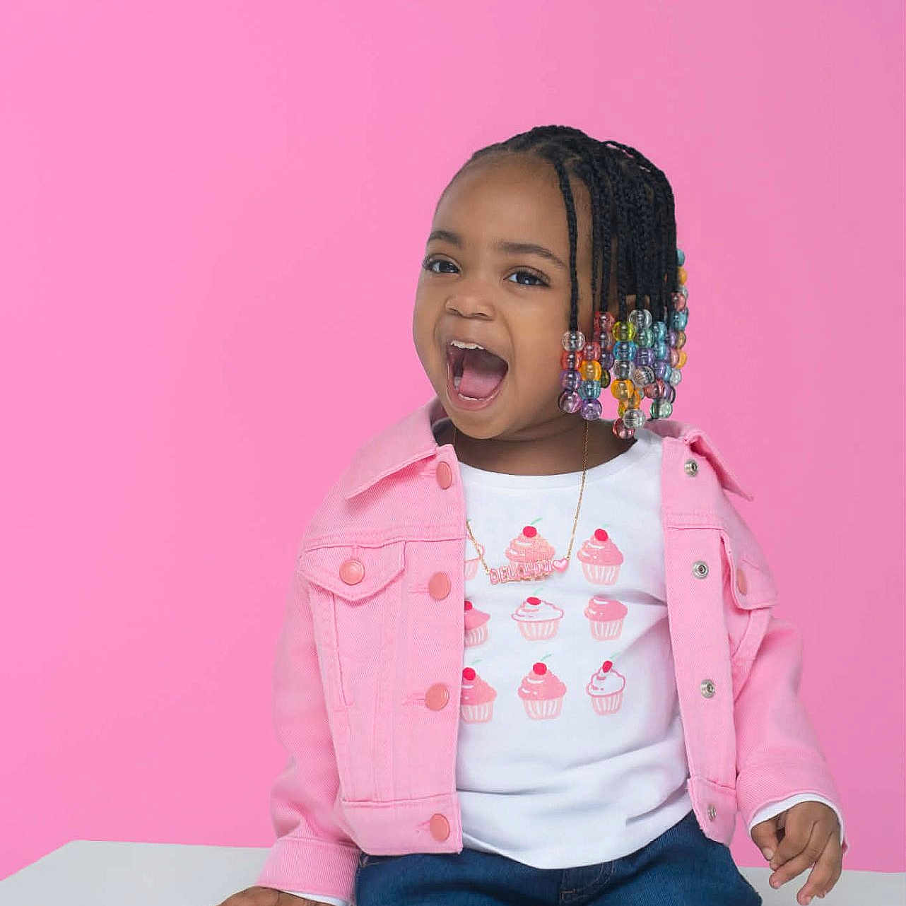 Delahni joined the competition — help win amazing prizes! child, girl, smiling, pink_jacket, denim_skirt, white_tights, beaded_hair, colorful_beads, happy, studio, pink_background, portrait, sitting, fashion, cute, jewelry, playful, young_child, casual_clothing, joyful