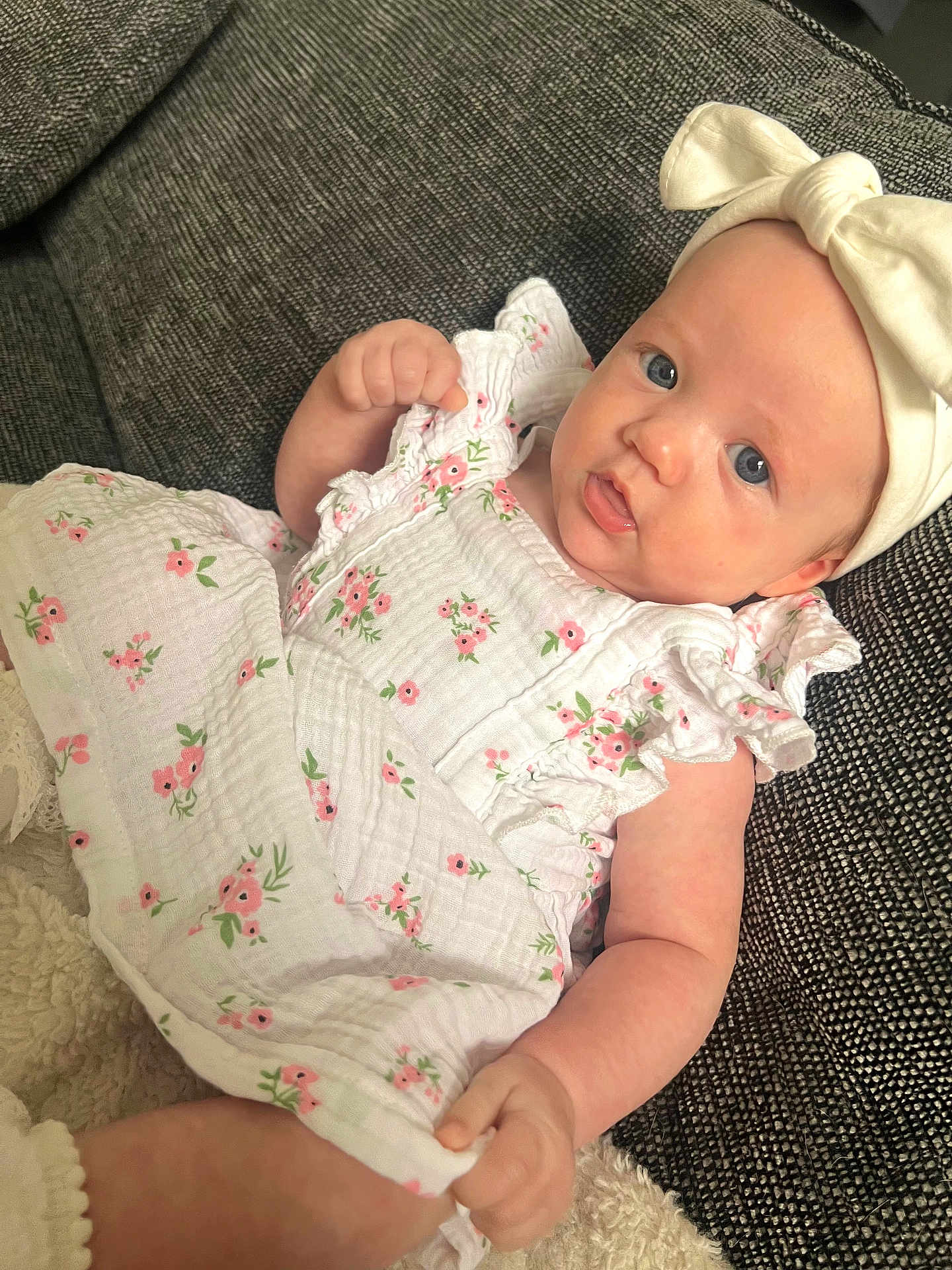 Isla joined the competition — help win amazing prizes! baby, infant, child, dress, headband, bow, flower_pattern, blue_eyes, couch, textured_fabric, comfortable, cute, smiling, hand, legs, skin, indoors, portrait, closeup, relaxed
