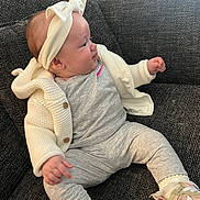 Isla joined the competition — help win amazing prizes! baby, child, headband, bow, sneakers, grey_clothing, knitwear, couch, seated, infant, cute, cozy, indoor, portrait, side_view, young_child, textile, footwear, smiling, person