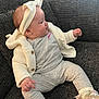 baby, child, headband, bow, sneakers, grey_clothing, knitwear, couch, seated, infant, cute, cozy, indoor, portrait, side_view, young_child, textile, footwear, smiling, person