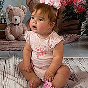 Gaia is registered to the contest to win money with this photo: baby, child, girl, crown, headband, flower_bracelet, pink_clothing, teddy_bear, plush_toy, sitting, floor, wood_texture, curly_hair, cute, indoor, portrait, decor, soft_lighting, expression, adorable