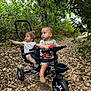 Gaia is registered to the contest to win money with this photo: toddler, child, tricycle, outdoor, forest, leaves, nature, path, greenery, baby, toy, play, vehicle, seat, handlebar, expression, clothing, footwear, adventure, person