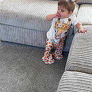 Gaia is registered to the contest to win money with this photo: toddler, child, indoor, carpet, couch, striped_couch, giraffe_outfit, pigtails, curious, standing, furniture, home, cozy, cute, person, young_child, clothing, patterned_pants, portrait, baby
