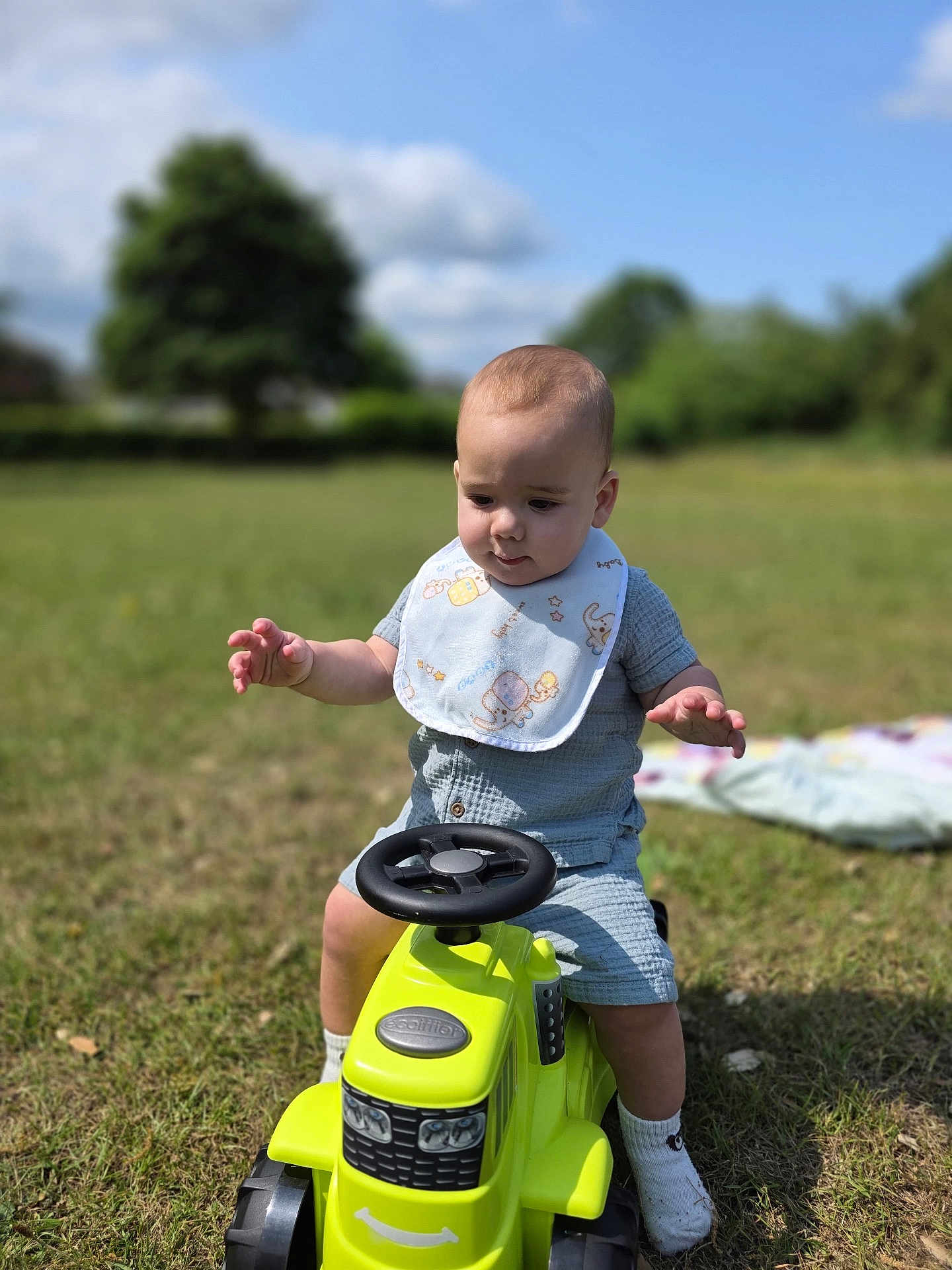 Roman joined the competition — help win amazing prizes! baby, child, toy, tractor, outdoor, grass, bib, blue_sky, greenery, sunlight, socks, playing, cute, infant, one_person, summer, nature, daytime, portrait, happy