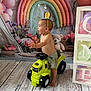 toddler, child, toy_tractor, crown, bubbles, rainbow, teddy_bear, flowers, playroom, balloons, wooden_floor, barefoot, shorts, smiling, indoor, decorations, cute, happy, person, portrait