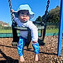 toddler, child, swing, playground, hat, blue_sky, sunny, outdoor, fence, wood_chips, clothing, pants, baby_swing, barefoot, person, daylight, play, seat, chain, curious
