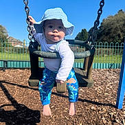 Roman joined the competition — help win amazing prizes! baby, barefoot, blue_sky, chains, child, dinosaur_pattern, fence, grass, hat, outdoor, pants, person, play, playground, seat, shadow, sunny, swing, tree, wood_chips