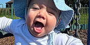 Roman is registered to the contest to win money with this photo: baby, blue_sky, child, cute, daylight, fence, greenery, happy, hat, infant, joyful, metal_chain, outdoor, person, playground, smiling, sunhat, swing, white_shirt, wood_chips