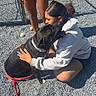 animal, casual_clothing, dog, fence, friendship, frisbee, grass, gravel, hoodie, hugging, interaction, leash, outdoor, person, pet, playful, shadow, shorts, sunlight, tennis_ball