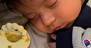 Gael joined the competition — help win amazing prizes! baby, sleeping, infant, portrait, peaceful, pacifier, cozy, blanket, clothing, sweater, champion_logo, close_up, face, dark_hair, indoors, resting, snuggled, soft_lighting, vertical_photo, nap