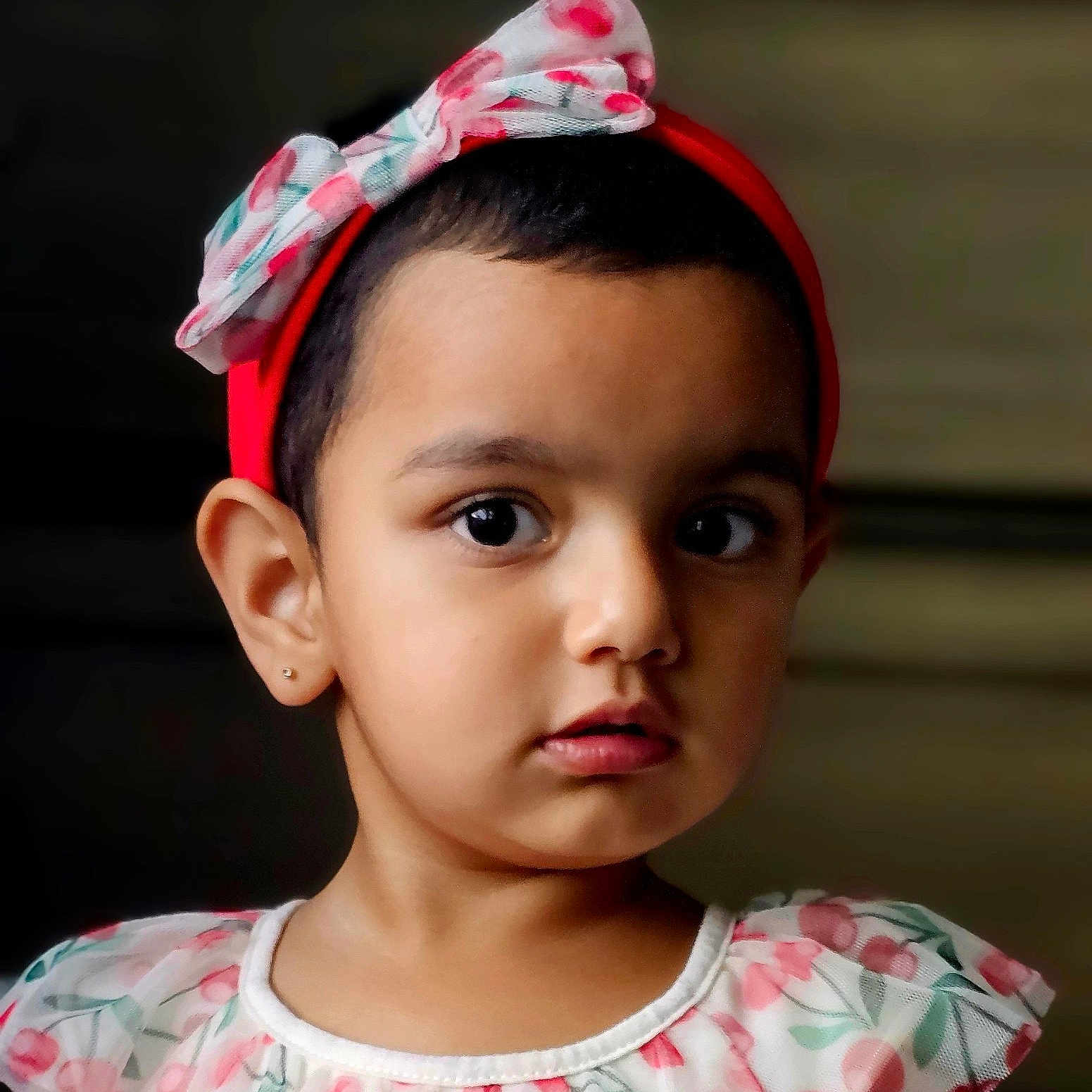 Kaeya is registered to the contest to win money with this photo: bow, child, closeup, clothing, dark_background, dress, earring, eyes, face, fashion, floral_dress, girl, hair, headband, indoors, person, photography, portrait, serious, toddler