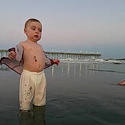 Lincoln is registered to the contest to win money with this photo: toddler, child, beach, water, pier, sunset, pants, shirt, dirt, sand, reflection, ocean, waves, sky, light, curious, standing, outdoor, nature, casual