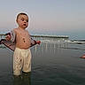toddler, child, beach, water, pier, sunset, pants, shirt, dirt, sand, reflection, ocean, waves, sky, light, curious, standing, outdoor, nature, casual