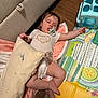baby, sleeping, pacifier, onesie, pillow, blanket, play_mat, toy, floor, couch, infant, child, wooden_floor, head, face, hand, foot, cozy, indoor, adorable