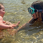 Madelyn is registered to the contest to win money with this photo: child, baby, water, lake, splash, goggles, swimming, fun, outdoor, sunlight, happy, play, summer, nature, person, legs, reflection, shallow_water, trees, recreation