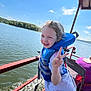child, life_jacket, peace_sign, boat, lake, water, outdoor, smiling, girl, summer, sunny, nature, trees, recreation, adventure, happy, person, blue_sky, water_splash, casual_clothing