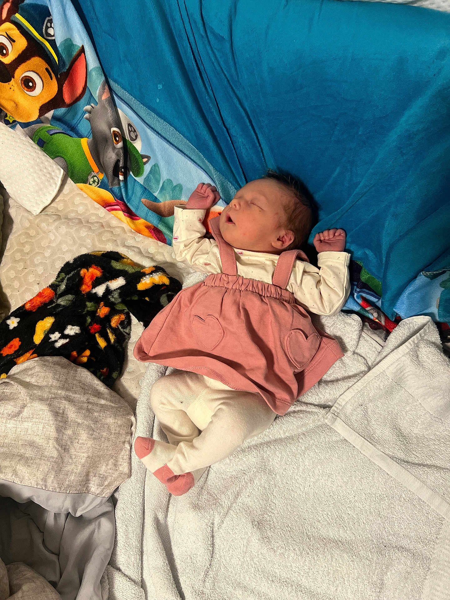 Barbra is registered to the contest to win money with this photo: baby, newborn, sleeping, pink_dress, heart_pockets, socks, blanket, paw_patrol, towel, pillow, bed, indoor, infant, portrait, cozy, resting, cute, soft_textiles, colorful, small_hands