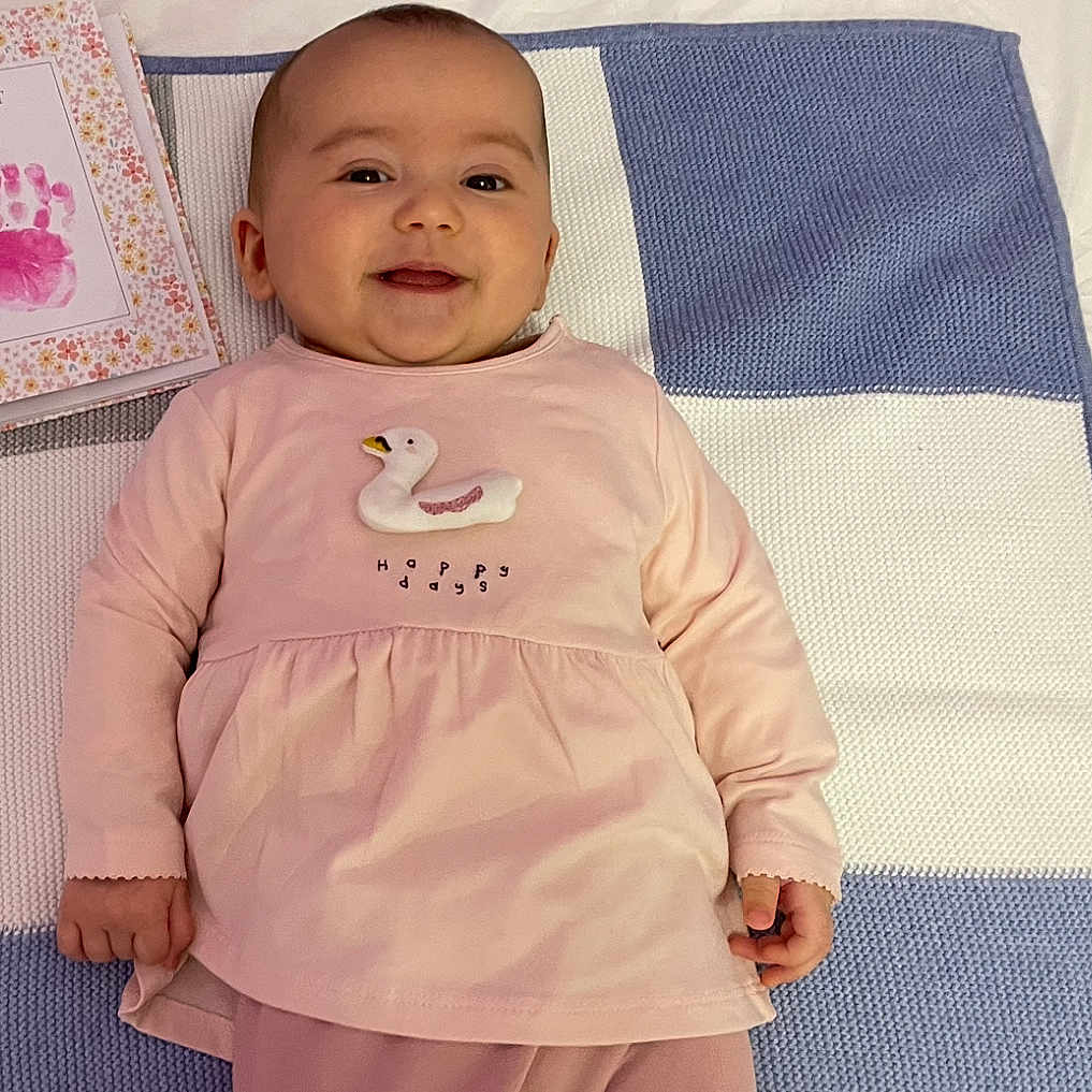 Aria is registered to the contest to win money with this photo: applique, baby, blanket, bodypart, clothing, coat, cushion, face, finger, furniture, hand, happy, head, longsleeve, pattern, person, photography, portrait, sleeve, smile