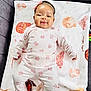 baby, child, smiling, pajamas, floral_pattern, blanket, headband, bow, couch, soft_toy, patterned_blanket, indoor, cute, happy, lying_down, infant, cozy, comfort, portrait, person