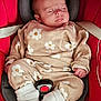 baby, sleeping, car_seat, red, beige, flower_pattern, clothing, white_socks, infant, child, cute, peaceful, seatbelt, head_support, portrait, indoors, soft_lighting, small_hands, cozy, resting
