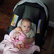 Emily joined the competition — help win amazing prizes! baby, doll, car_seat, blanket, indoor, child, infant, toy, pink, floor, wooden_floor, clothing, person, cute, holding, seat, comfort, young, baby_clothes, portrait