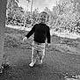 child, toddler, barefoot, black_and_white, outdoor, walking, tongue_out, grass, trees, nature, path, casual_clothing, smiling, young_child, person, playful, daylight, happy, cute, portrait