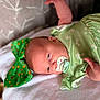 baby, infant, newborn, pacifier, green_outfit, floral_pattern, lying_down, blanket, bedding, head, face, eyes_open, hand, pillow, bow, soft_texture, portrait, cute, nursery, skin