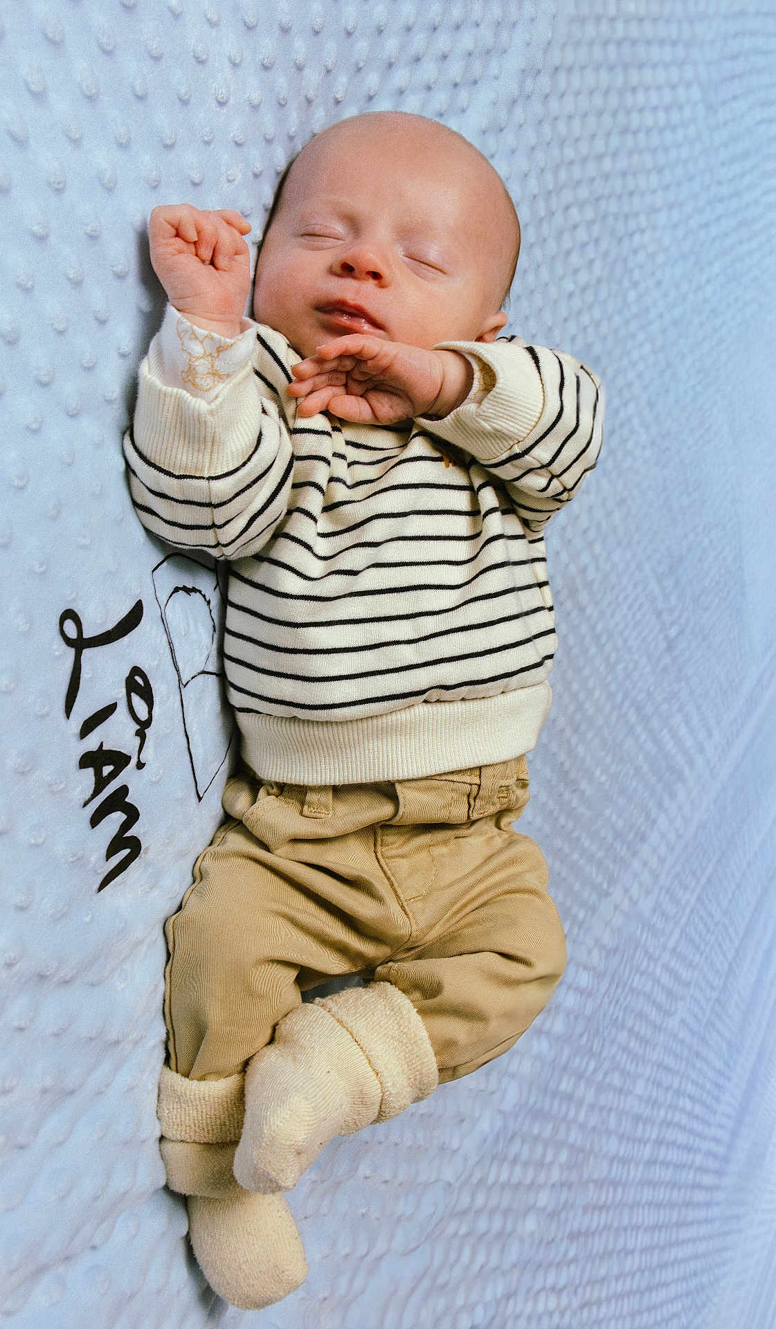 Liam a rejoint le concours — aidez-le/la à gagner de superbes lots ! baby, infant, sleeping, striped_sweater, beige_pants, socks, blanket, blue_background, cozy, cute, child, newborn, relaxed, soft_texture, portrait, indoor, warm_clothing, peaceful, small_hands, resting
