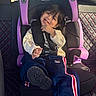 child, toddler, car_seat, graco, smiling, clothing, sweatshirt, pants, shoe, car_interior, seat_belt, quilted_leather, window, sunlight, hair, face, playful, cute, seat, sitting