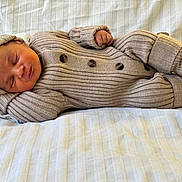 Nahel participe au concours pour gagner de l'argent avec cette photo : baby, infant, sleeping, knitted_outfit, hat, booties, cozy, beige, blanket, bed, peaceful, cute, newborn, soft_texture, resting, portrait, child, warm_clothing, indoor, comfort
