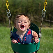 Luca is registered to the contest to win money with this photo: baby, child, daylight, fun, grass, green_swing, happy, holding, nature, outdoor, person, playground, playing, seat, smiling, summer, sunny, swing, toddler, yellow_chain