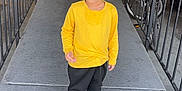 Fateh joined the competition — help win amazing prizes! child, boy, yellow_shirt, black_pants, red_sneakers, concrete, walkway, metal_railings, door, bicycle, outdoor, standing, hair, blue_eyes, expression, casual_clothing, urban, daylight, side_view, person