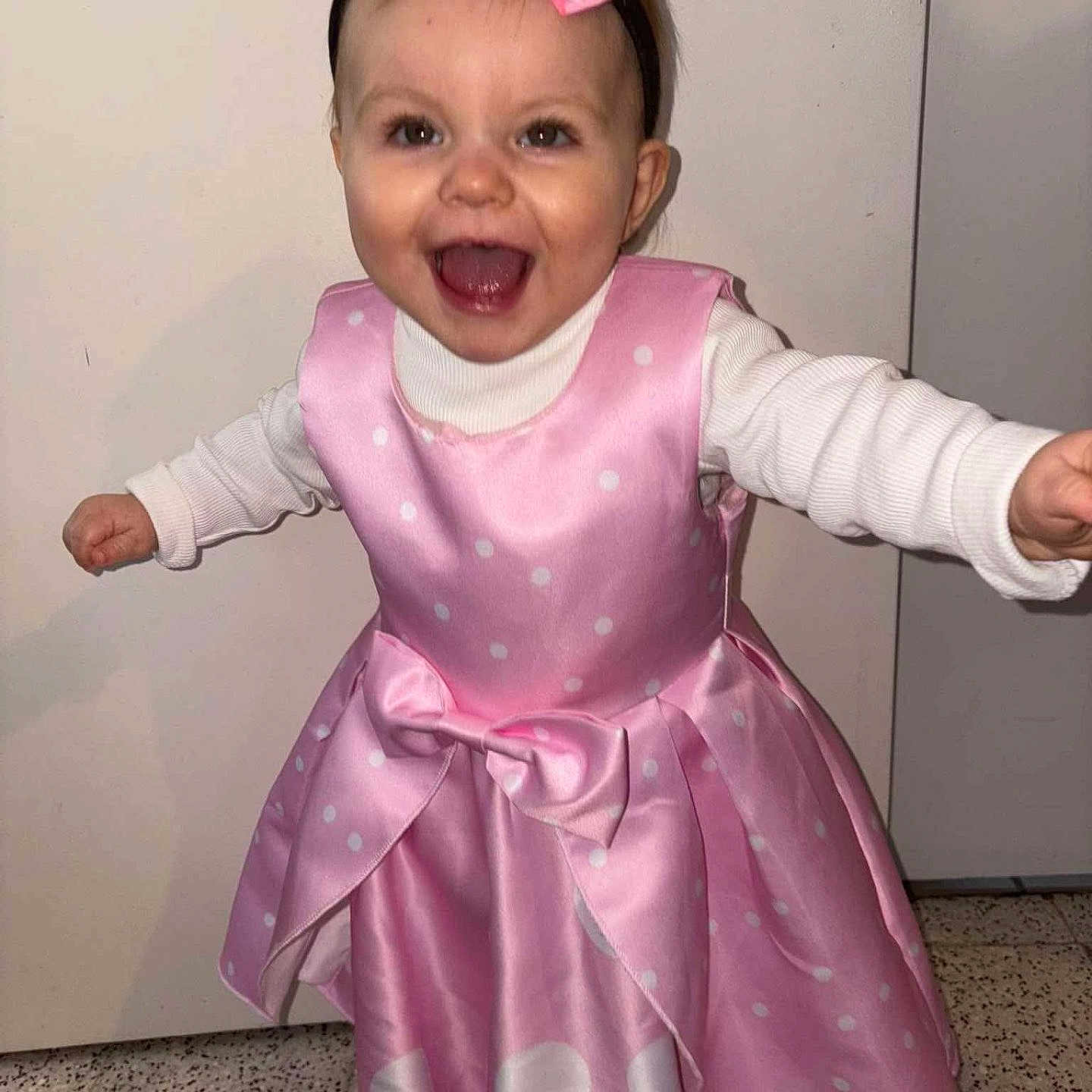 Noëlya participe au concours pour gagner de l'argent avec cette photo : arms_outstretched, bow, celebration, child, eyes, face, floor, hair, happy, headband, indoor, long_sleeve, mouth_open, person, pink_dress, polka_dot, smiling, standing, toddler, white_shirt