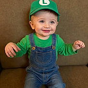 Mazen joined the competition — help win amazing prizes! baby, cap, casual, child, clothing, couch, cute, denim_overalls, face, green_hat, green_shirt, happy, headwear, indoors, person, portrait, sitting, smiling, toddler, young_child