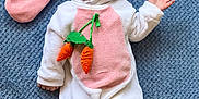 Mazen is registered to the contest to win money with this photo: baby, bunny_costume, pink_ears, carrot_toy, blue_blanket, smiling, waving_hand, cute, infant, soft_texture, lying_down, child, hooded_outfit, plush, happy_face, costume, indoors, person, portrait, cozy
