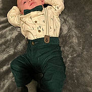 Mazen is registered to the contest to win money with this photo: baby, infant, clothing, bow_tie, suspenders, pants, shirt, sock, blanket, lying_down, cute, portrait, soft_texture, indoors, child, young, person, apparel, comfort, relaxing