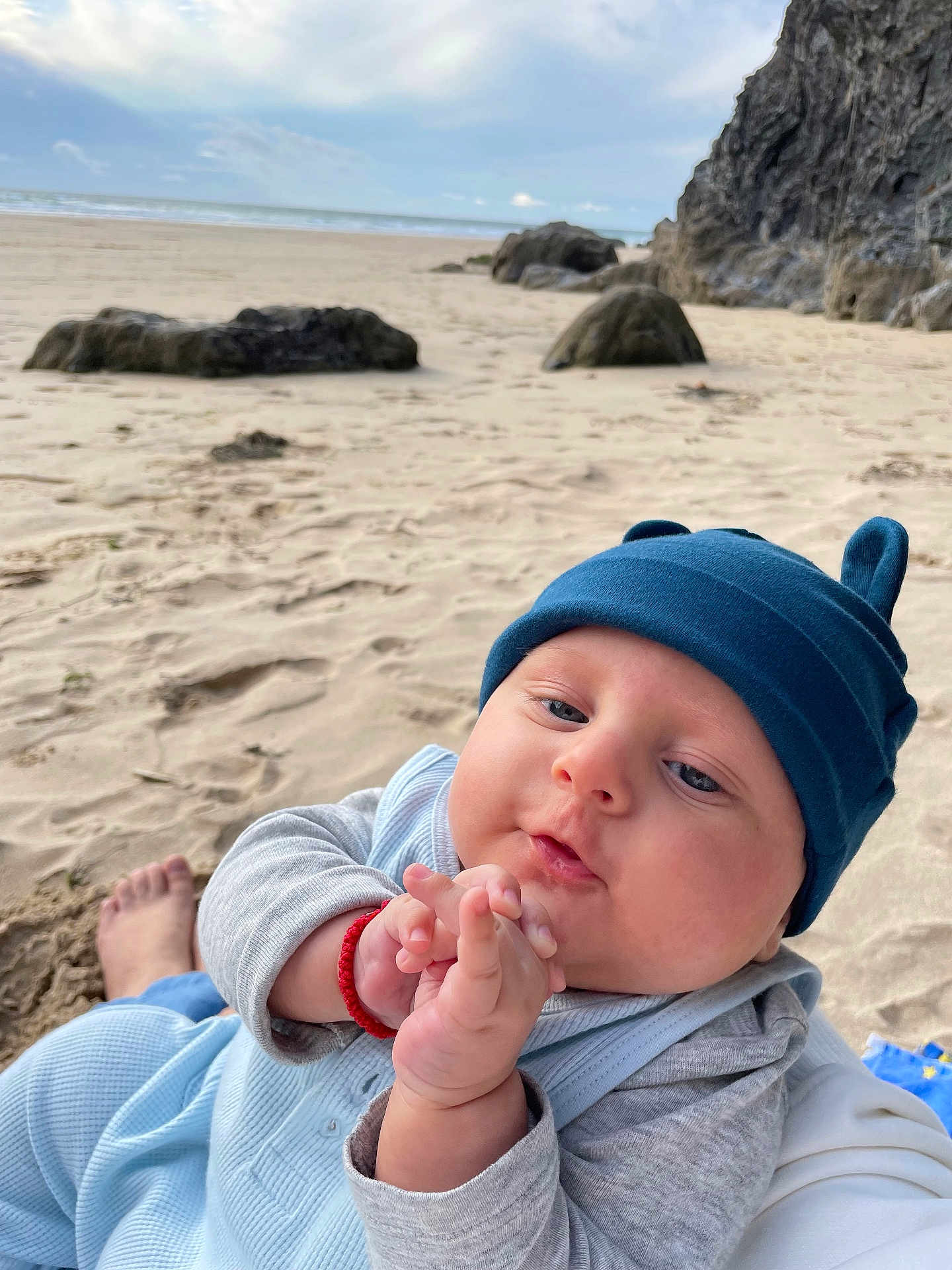 Victor joined the competition — help win amazing prizes! baby, infant, blue_hat, sand, beach, rocks, sky, cloudy, hands, clothing, person, cute, outdoor, nature, portrait, child, closeup, headwear, casual, relaxed