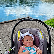 Jazmin is registered to the contest to win money with this photo: baby, car_seat, child, clouds, cute, greenery, headband, infant, lake, nature, outdoor, person, playful, sky, smiling, sunny_day, trees, water, waterfall, wooden_dock