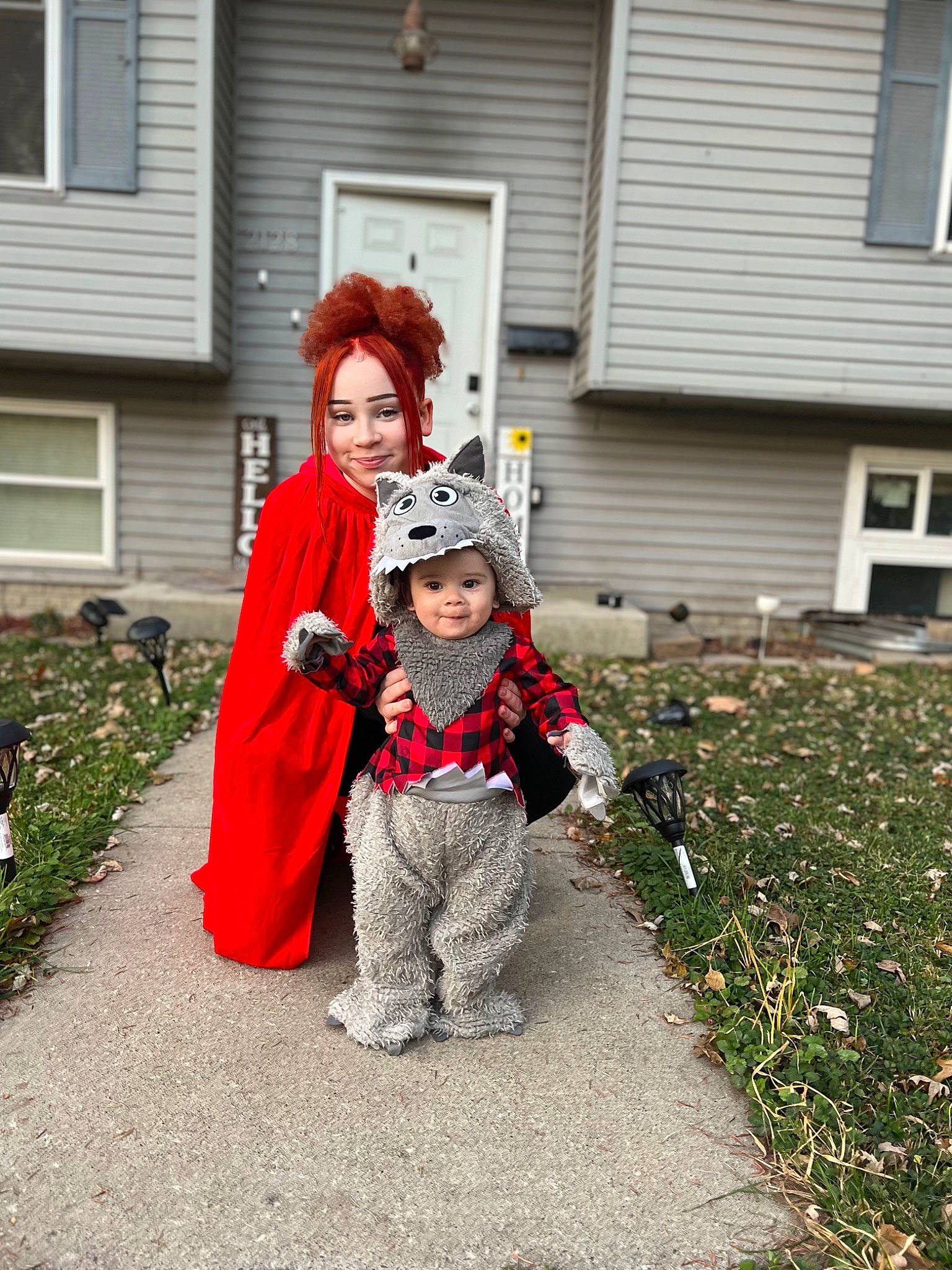 Khyree is registered to the contest to win money with this photo: carmine, coquelicot, costume, event, fun, fur, garden, grass, hat, headwear, house, joy, lawn_ornament, person, personal_protective_equipment, plant, pumpkin, recreation, sidewalk, toddler