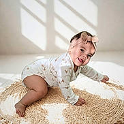 Aurora is registered to the contest to win money with this photo: baby, infant, crawling, onesie, headband, bow, smiling, happy, cute, indoor, rug, woven_rug, natural_light, shadow, playful, child, person, floor, home, soft_light