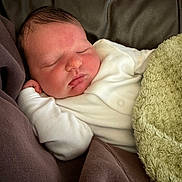 Hudson is registered to the contest to win money with this photo: baby, blanket, child, closed_eyes, comfort, cozy, cute, green_blanket, indoors, infant, leather_surface, newborn, peaceful, portrait, resting, sleeping, small_hands, soft_texture, warm, white_clothing